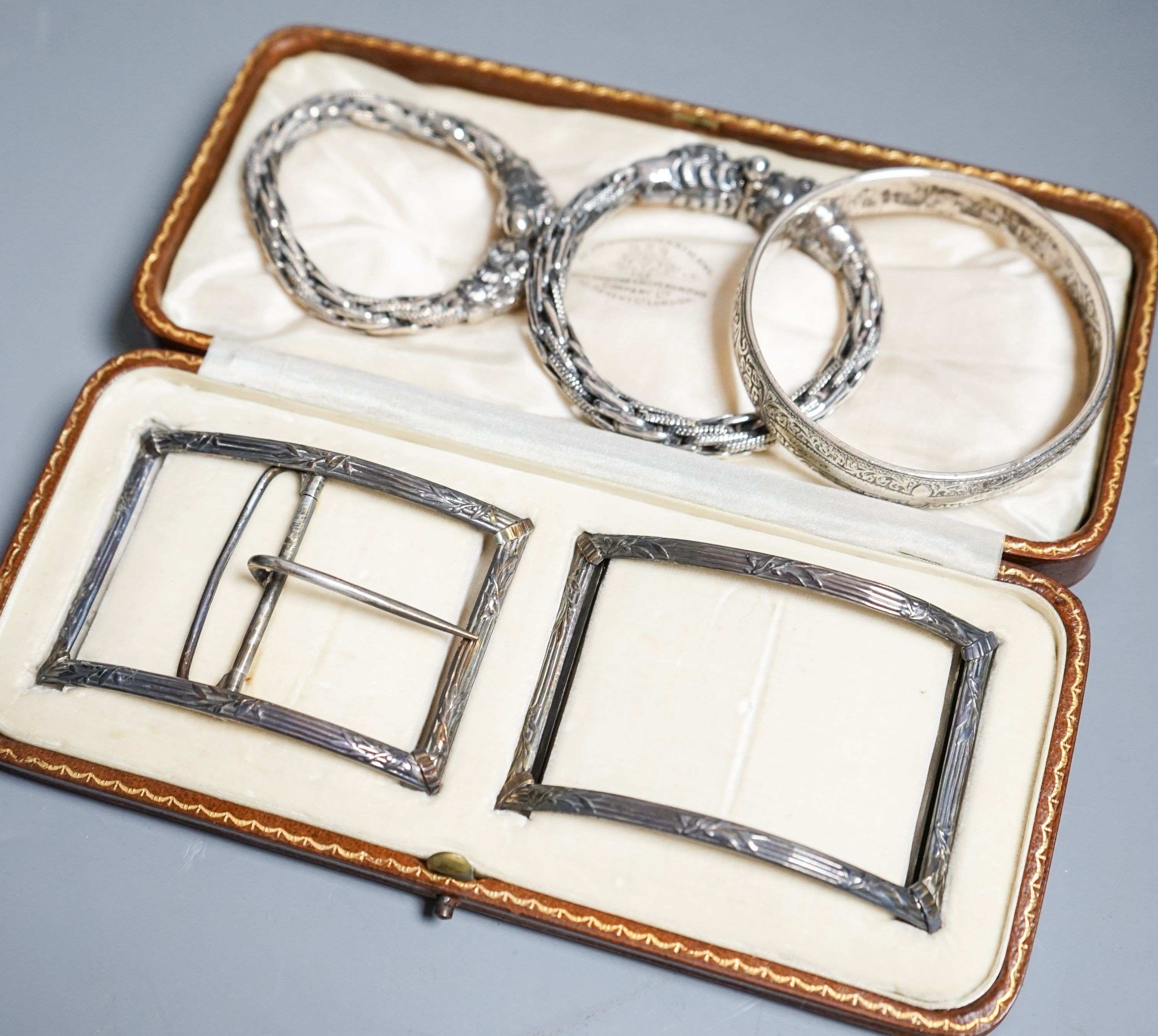 A cased Edwardian belt buckle, Goldsmiths & Silversmiths Co Ltd, London, 1908 and three bangles.